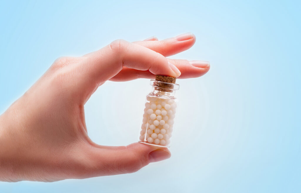Homeopátiás golyókat tartalmazó üveget fogó kéz.
