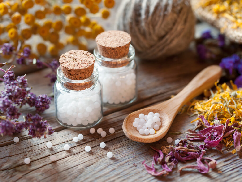Homeopátiás golyócskák üvegei, fakanál és száraz egészséges gyógynövények. Szelektív fókusz.