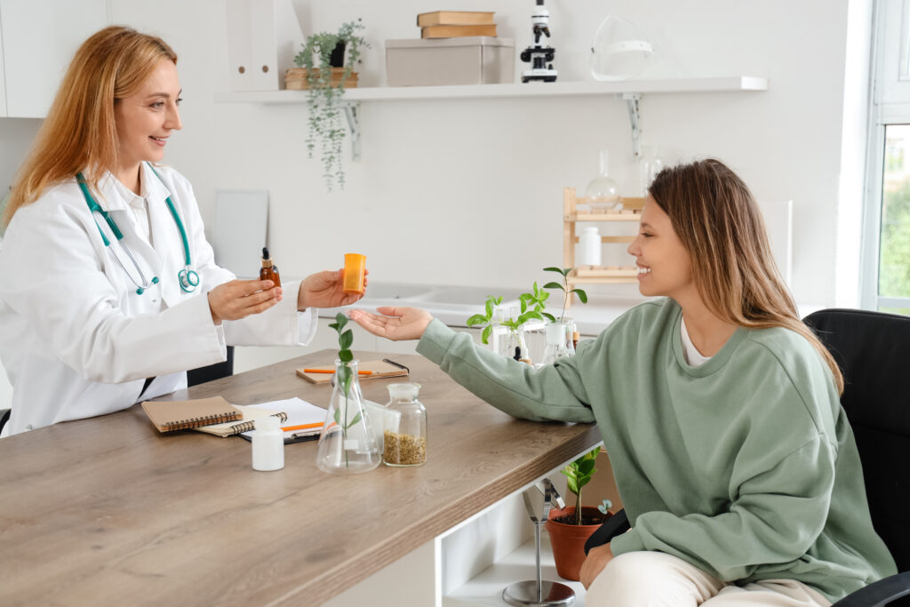 Fiatal nő homeopata orvosnál ül. Kezébe homeopátiás készítményt tart.