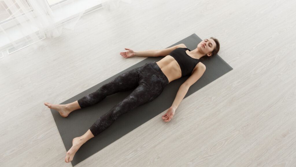 Nyugodt lány pihentető savasana pózban a szőnyegen otthoni edzés után.