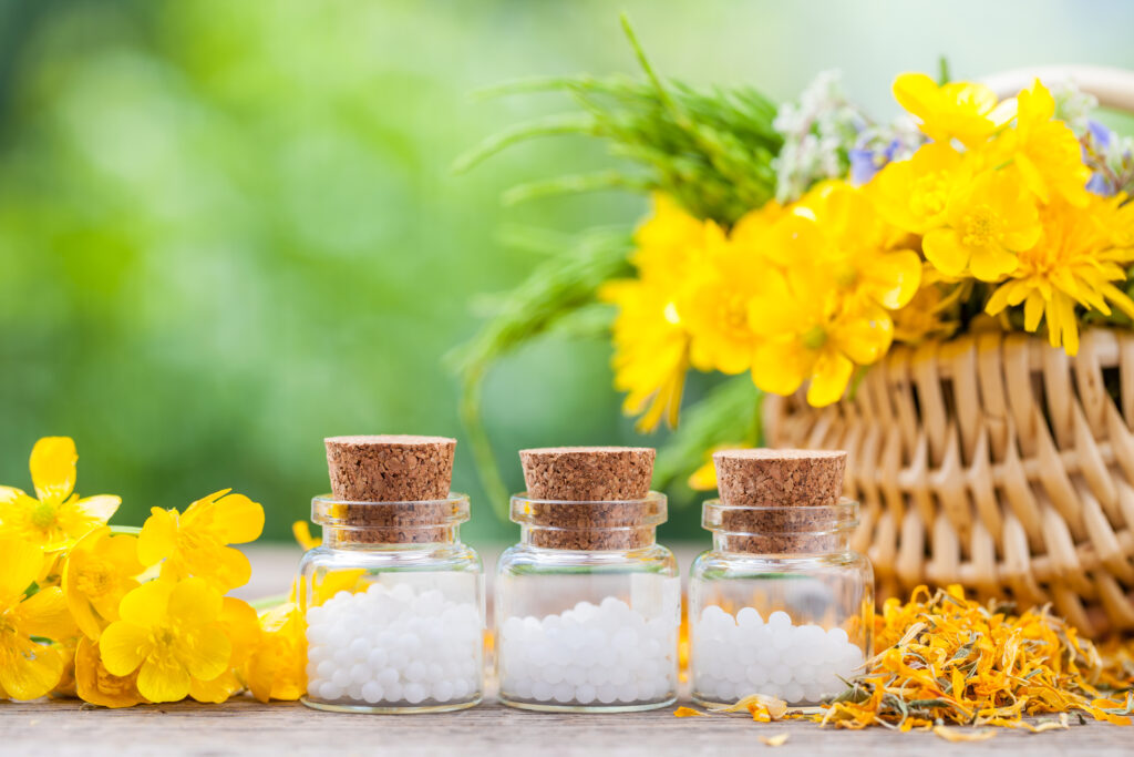 Arnica homeopátiás szerek kis üvegekben a virágok mellett.