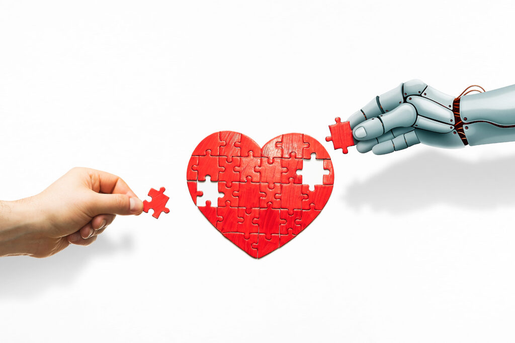 Emberi kéz és egy robot kéz együtt rak ki egy szív puzzle-t.