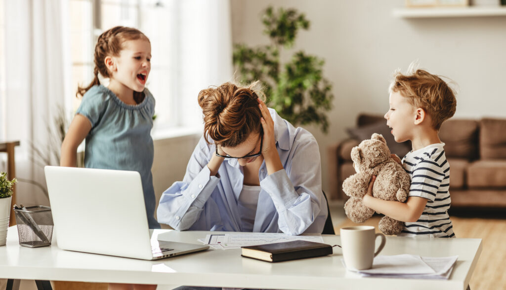 Kis huncut gyerekek zajonganak és zavarják a szabadúszó anya figyelmét, miközben próbál a laptopjára koncentrálni, nő benne a stressz, és a fejét szorítva dolgozik.
