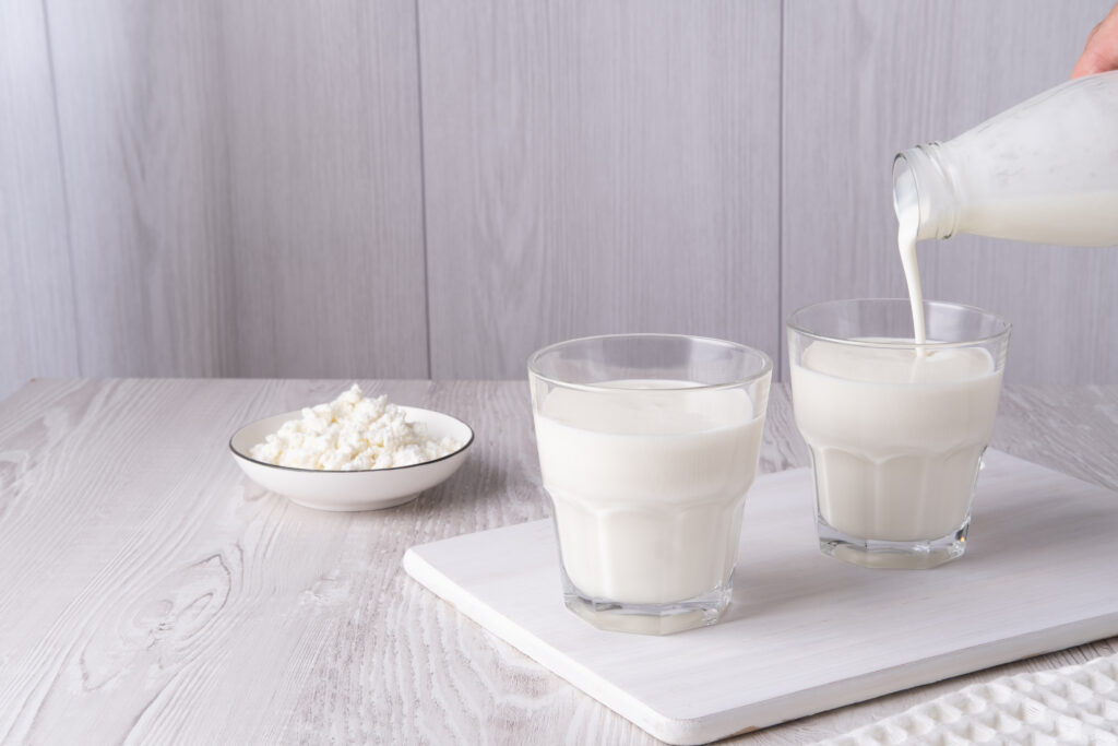 Otthoni kefir, író vagy probiotikus joghurt öntése. Joghurt folyik egy üvegből világos háttér előtt. Probiotikus hidegen erjesztett tejital. Divatos étel és ital. Üres hely.