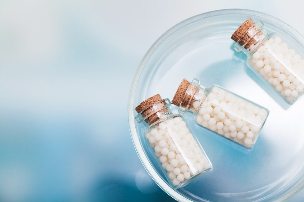 Homeopátiás golyókkal telt üvegcsék kék háttér előtt.
