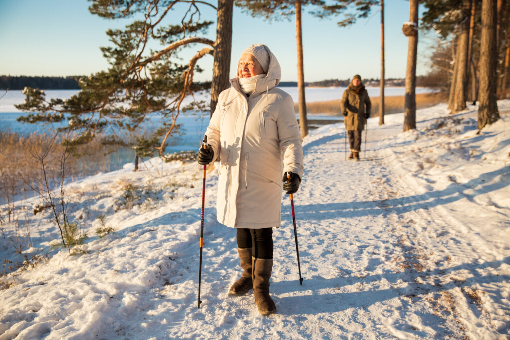 Nordic walking téli tájban. Idősebb nő kirándul bottal a kezében a téli erdőben.