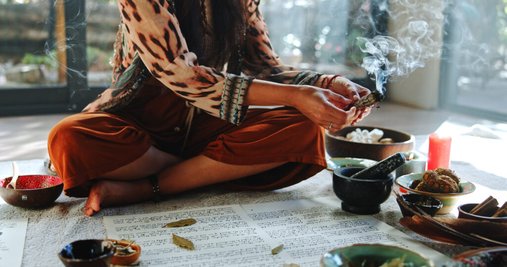 Nő törökülésben ülve készül fel a meditáláshoz, miközben gyógynövényből készült füstölőt éget.