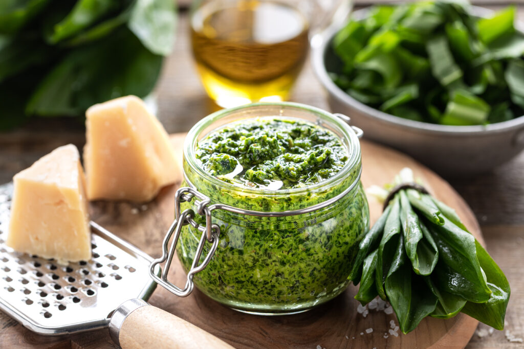 Medvehagyma pesto üvegben sajttal és sajtreszelővel fa tányéron.