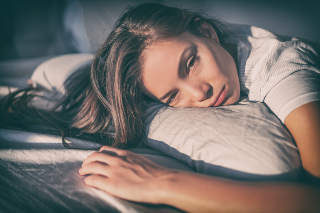 Depresszió, energiahiány, rossz kedv. Fiatal nő fekszik az ágyon és maga elé néz üveges szemmel.