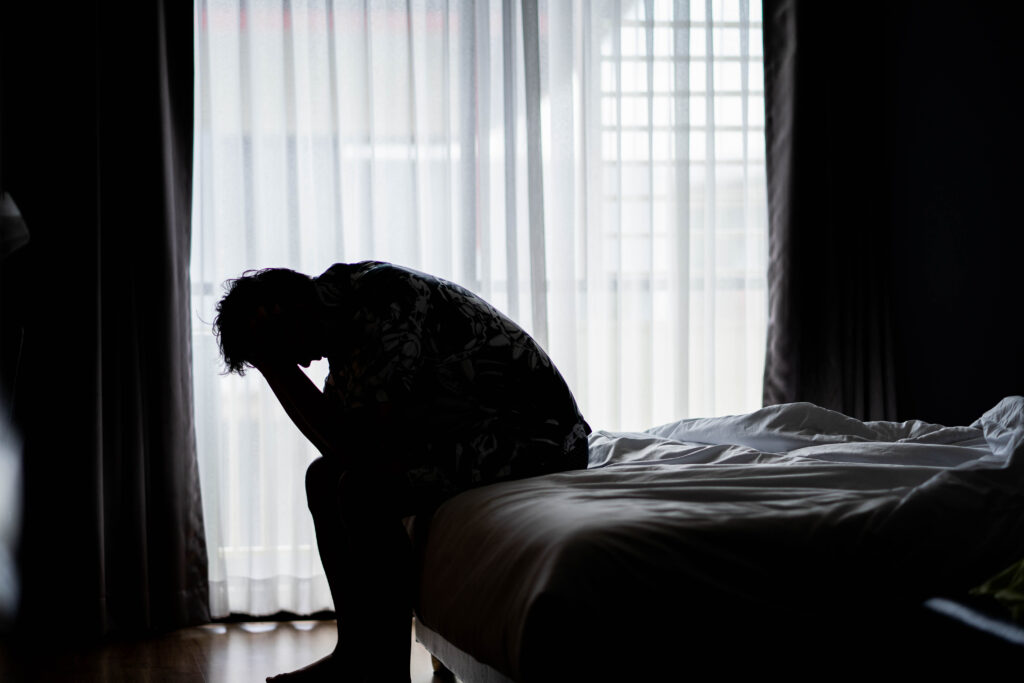 Férfi ül az ágyán, fogja a fejét. Szomorú, beteg, depressziós.
