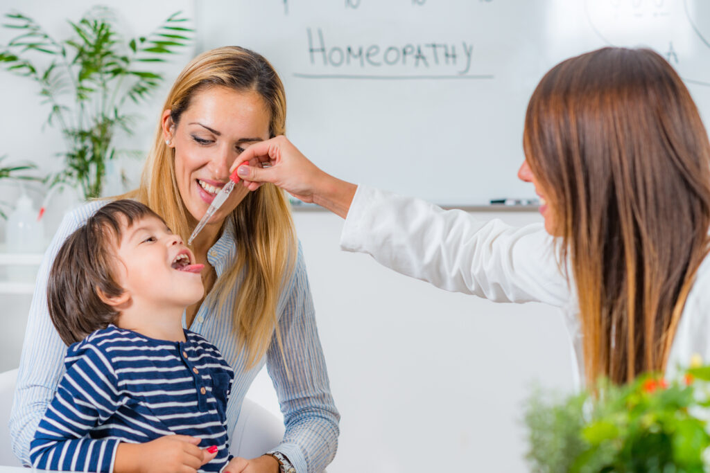 Kisfiú homeopátiát kap a gyerekorvostól, miközben az anyukája ölében ül.