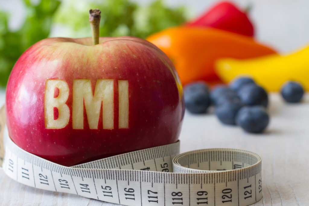 BMI testzsír mérés jele almába karcolva, előtte mérőszalag, mögötte gyümölcsök.